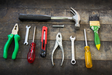 "Closeup flat lay of tools (hammer,
pliers,wrench,paint brushes,cutter) on a wooden surface texture"
