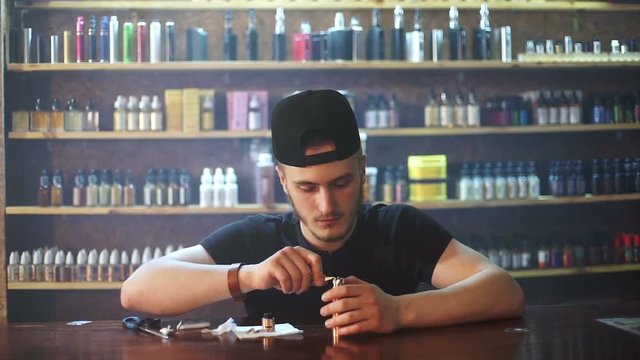 young seller in vape shop is installing cotton in atomizer show window in background