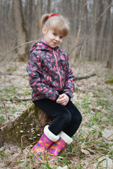 Fototapeta premium Portrait of a smiling young girl sitting on a stump in the spring forest