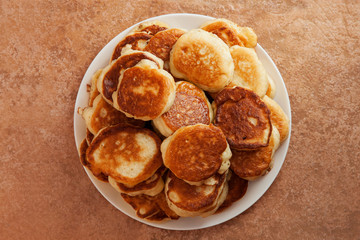 Stack of fried pancakes on a white plate, standing on a stone countertop. View from above