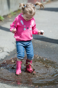 Little girl in rubber boots in buddle