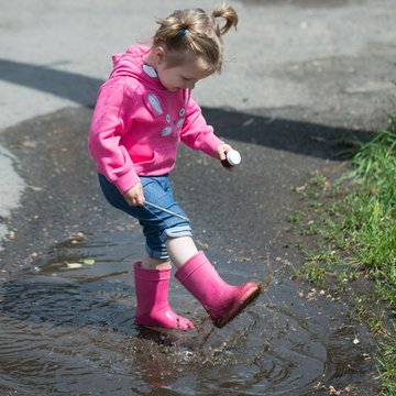 Little girl in rubber boots in buddle
