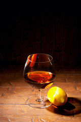 Glass of cognac with lemon on wooden background