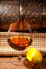 Glass of cognac with lemon on wooden background
