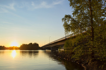 Silent evening by the lake in Finland. Image taken during sunset. A long bridge is on the right side next to a path.
