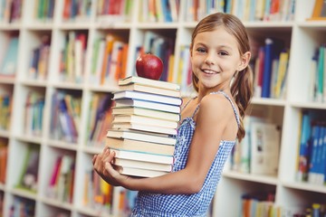 School girl holding stack of books in library
