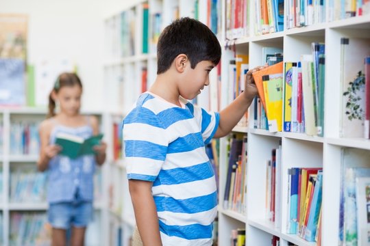 Boy taking a book from bookshelf in library