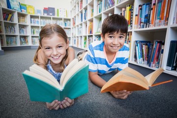 Happy school kids lying on floor and reading a book in library