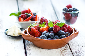 Delicious berries in a container with cream on a wooden background