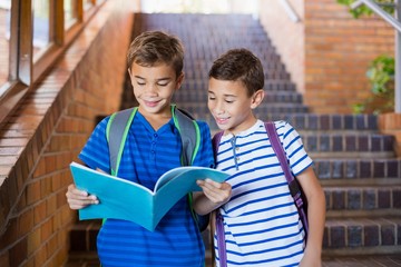 Smiling school kids reading a book on staircase