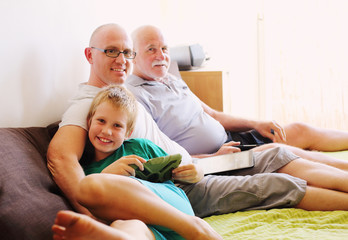 father, grandfather and son playing games on tablets and reading