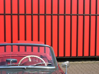 Cremefarbenes Lenkrad eines grauen deutschen Roadster der Fünzigerjahre vor rotem Industrietor im...