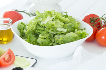 Preparing a healthy fresh salad with tomato, lettuce, cucumber and oil