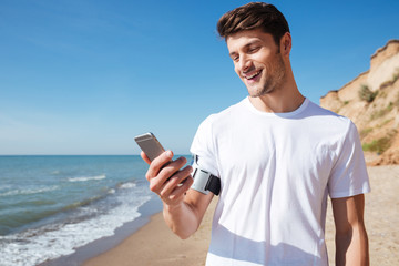 Cheerful young sportsman using smartphone on the beach
