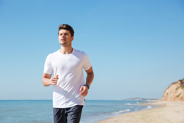 Concentrated young sportsman running on the beach