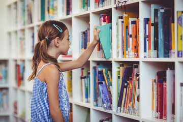 School girl taking a book from bookshelf in library