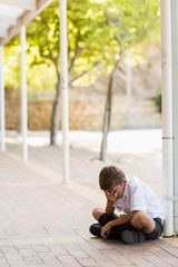 Sad schoolboy sitting alone in corridor