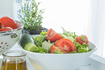Preparing a healthy fresh salad with tomato, lettuce, cucumber and oil