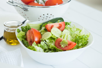 Preparing a healthy fresh salad with tomato, lettuce, cucumber and oil
