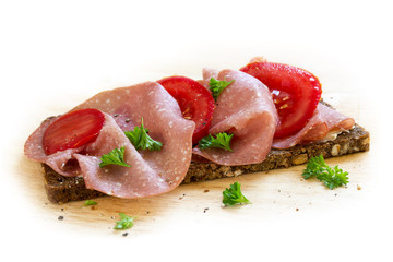 salami sausage and sliced tomato on a dark whole grain bread, background fades to white