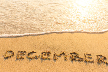 December - written on sandy beach with the soft wave.