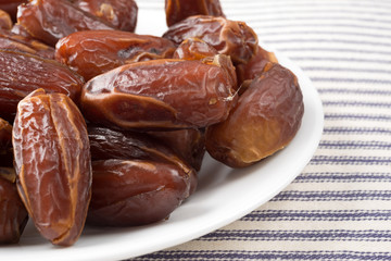 Tunisian pitted dates on a plate atop a blue striped tablecloth side close view.