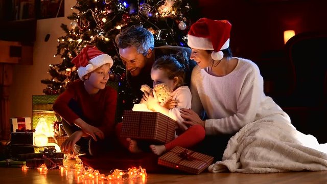 a family near the Christmas tree, the girl finds a teddy bear in her gift box
