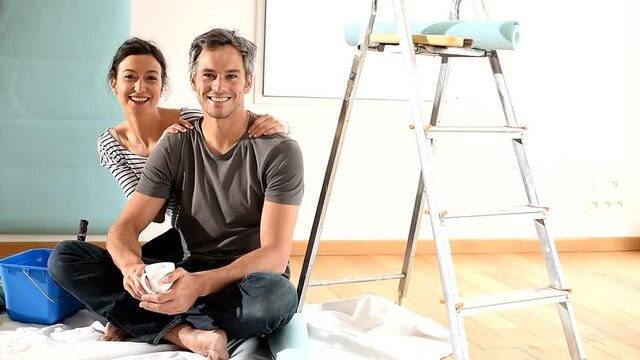 couple wallpapering their new flat taking a break drinking a cup of coffee
