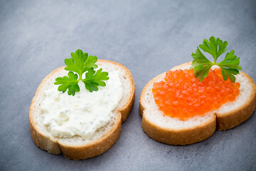 Bread with fresh cream cheese and red caviar on table.