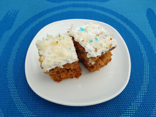 Two slices of cake, decorated on top with white cream, white plate, which stands on a blue tablecloth