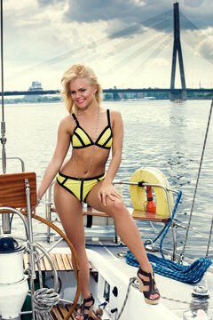 Young beautiful woman in yellow swimsuit driving the yacht at sunny day