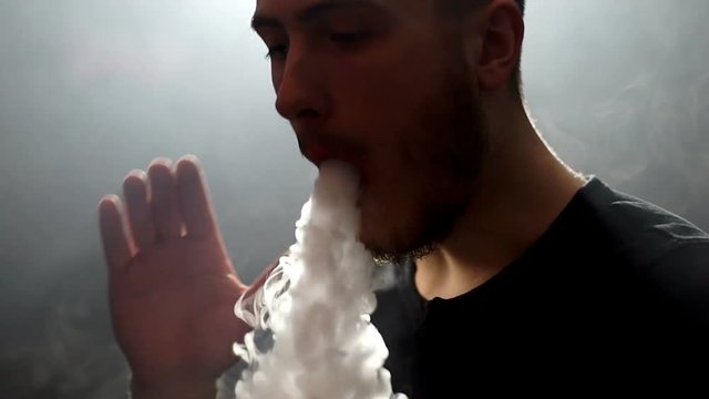 young vaper man exhaling big clouds of smoke with e-cigarette vape in slowmotion