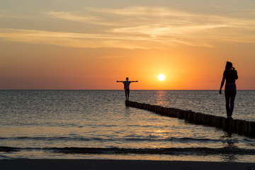 Fototapeta premium tow teenagers balancing on a groin at sunset