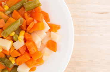 Close view of mixed vegetables on a white plate atop a wood table top close view.