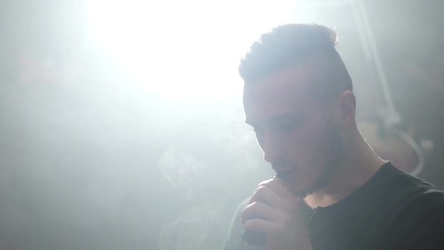 young vaper man exhaling big clouds of smoke with e-cigarette vape in slowmotion