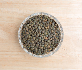 Fototapeta na wymiar Green lentils in a small bowl on a wood table top view.