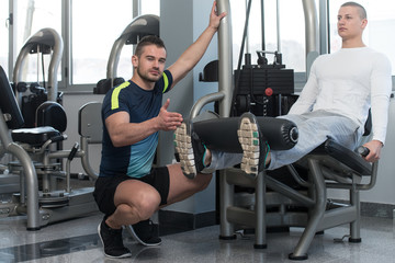 Fototapeta na wymiar Man Train Legs On Machine With Personal Trainer
