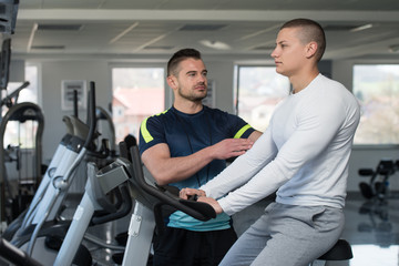 Personal Trainer Helping Client On Bicycle