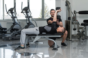 Fototapeta na wymiar Gym Coach Helping Man On Chest Exercise