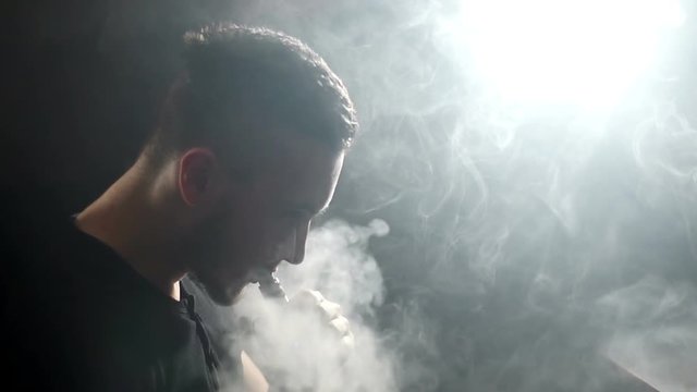 young vaper man exhaling big clouds of smoke with e-cigarette vape in slowmotion