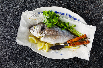 grilled fish, fresh parsley and cutlery for fish. on a marble ta