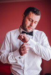 The groom in white shirt put his bow-tie in the morning of the wedding day. Close up photography. Preparation time