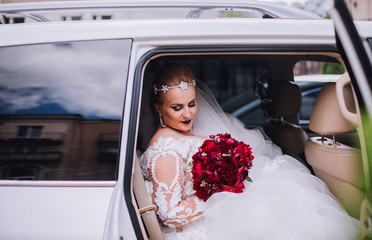 Portrait of a beautiful blonde bride sitting in the wedding car and looking at somebody or something through the window. Wedding day. Daylight