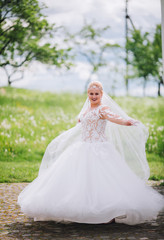 Fototapeta premium Young beautiful bride plays a wedding dress. Dress develops in the wind. Happy bride in a wedding dress is spinning.