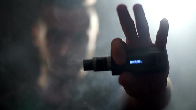 young vaper man exhaling big clouds of smoke with e-cigarette vape in slowmotion