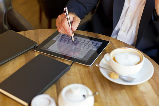 Businessman sitting in a coffee shop using digital tablet, partial view