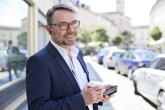 Portrait of smiling businessman with coffee to wearing earphones