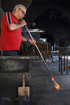 Man blowing with a tube molten glass in a glass factory