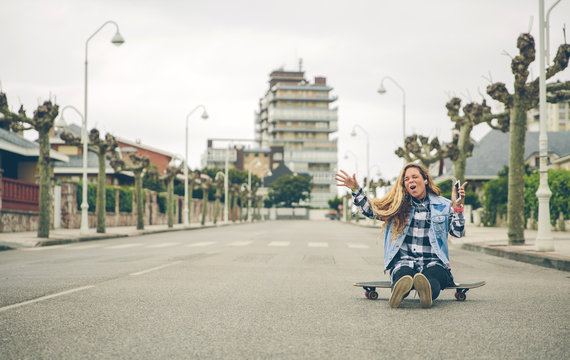 Carefree young woman listening to music sitting on skateboard