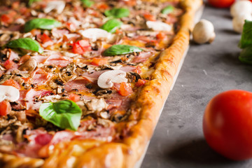 square pizza with basil tomatoes and mushrooms on a wooden board.  Pizza on the gray table